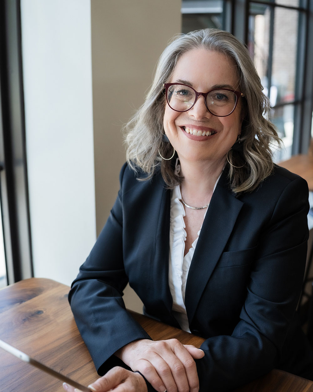 Lynda Grodd in suit at a table with tablet in hands