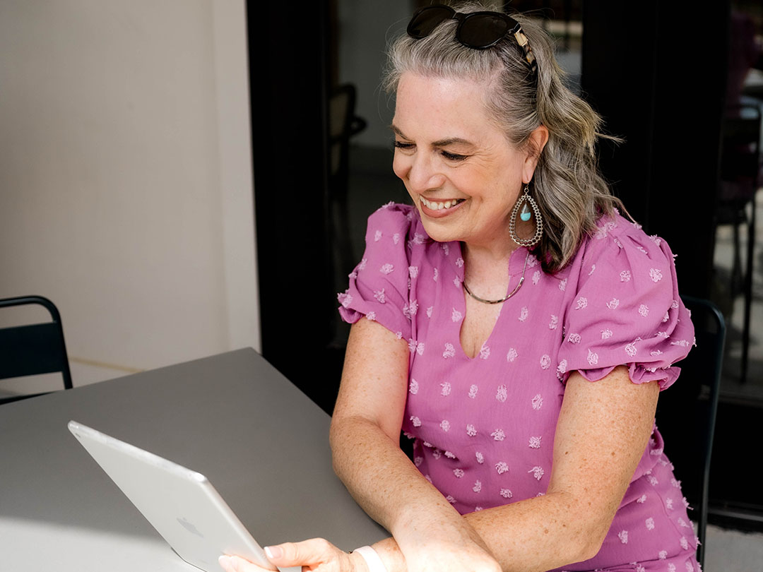 Lynda Grodd sitting at a table with tablet in hands